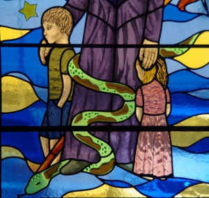 stained glass window of robed man with hands on two children and snake coiled around him