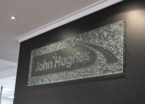 kiln formed sign of john hughes logo on black wall