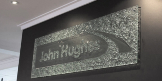 kiln formed sign of john hughes logo on black wall