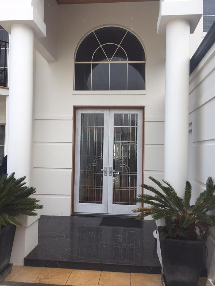 mansion entry with double glass doors in an art deco style and large arched window above