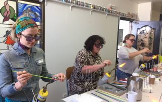 three students learning bead making over mapp gas flames