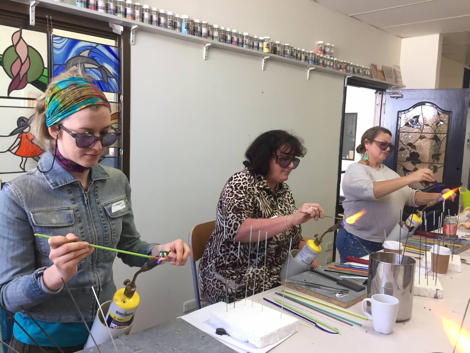 three students learning bead making over mapp gas flames