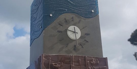 founders memorial made of metal obelisk clock with blue kiln formed glass top and low relief war imagery