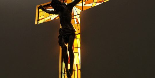 cast of jesus being back lit by stained glass cruciform window
