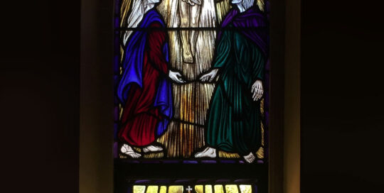 stained glass window with jesus in upper arched window and shield in lower window