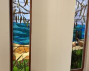 two panels of stained glass in unfinished room. The panels depict australian flora and fauna with sky, ocean, sand and scrub