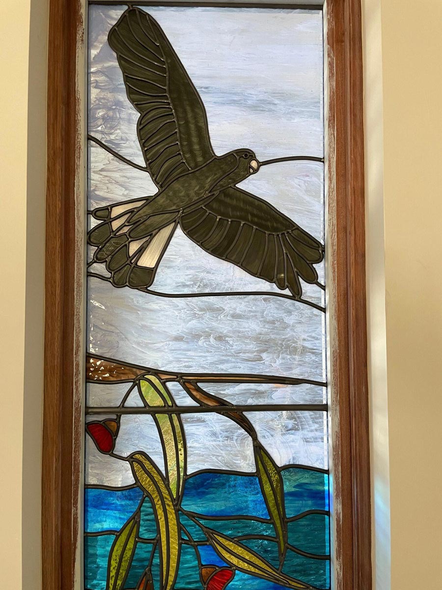 stained glass window depicting flying black cockatoo in Australian landscape