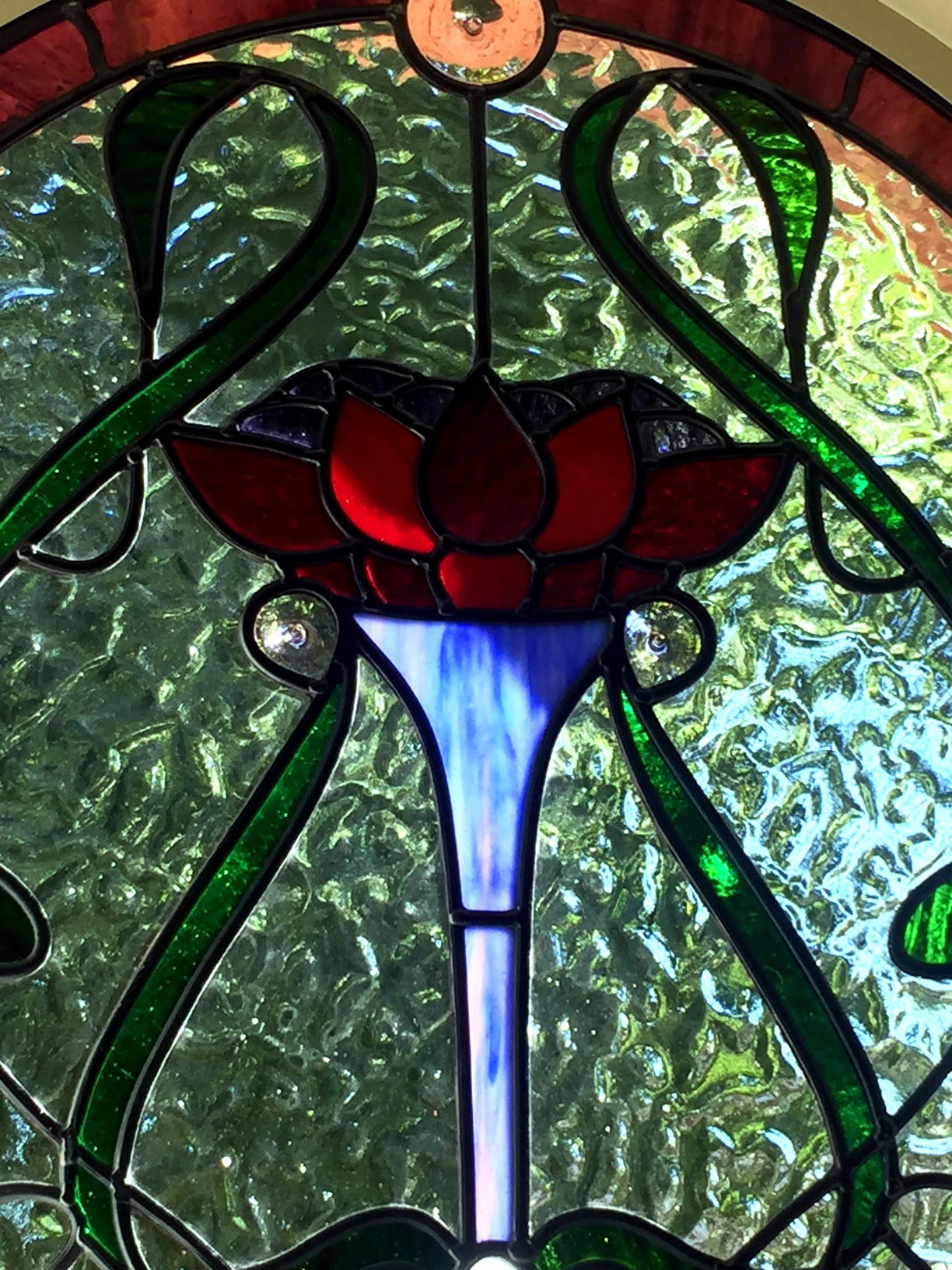 close up of art nouveau designed stained glass window showing red flower, blue stem and green surrounds.