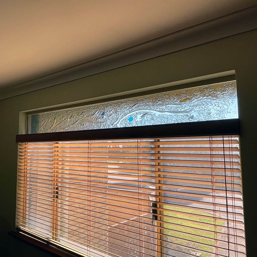 kiln formed window with laminated coloured pieces above window with wood venetian blinds