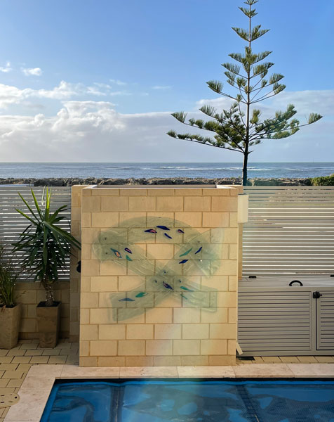 glass art work on limestone brick wall with pool in foreground and beach behind