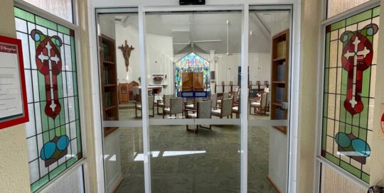 chapel seen through glass windows with a stained glass windows with crosses on each side