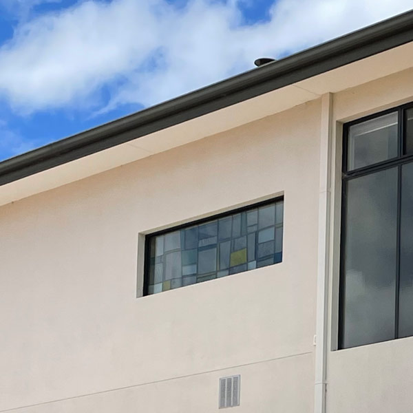 outside of house rendered wall and sky with two windows. One window has contemporary stained glass.