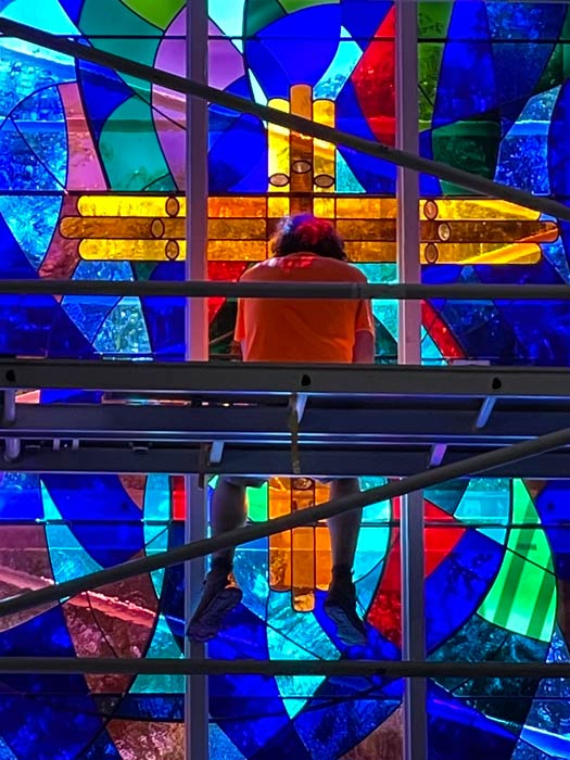 man sitting on scaffolding in front of colourful stained glass window
