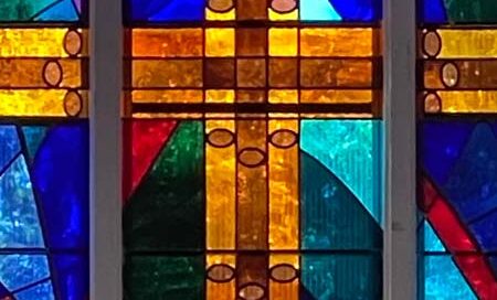 close up of three piece lancet window with yellow cross and blue green background