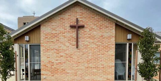 outside of church with crucifix on brick wall and lancet windows to sides