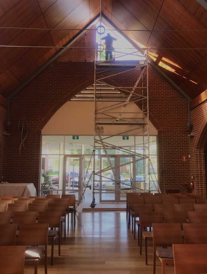 inside of church with man on scaffolding installing stained glass window