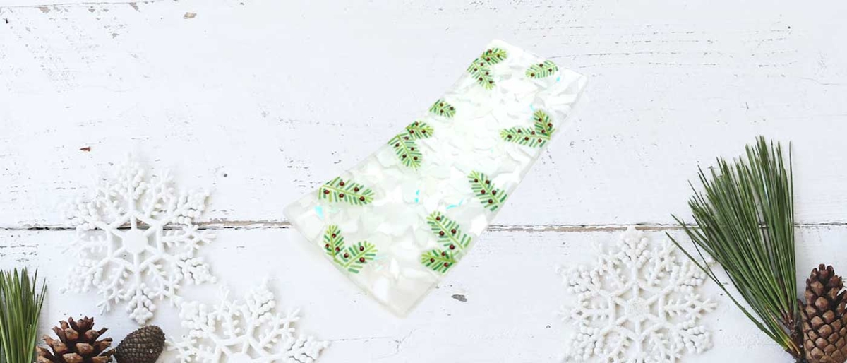 white snowflate glass platter with green pine leaf accents on background with pine needles and cones